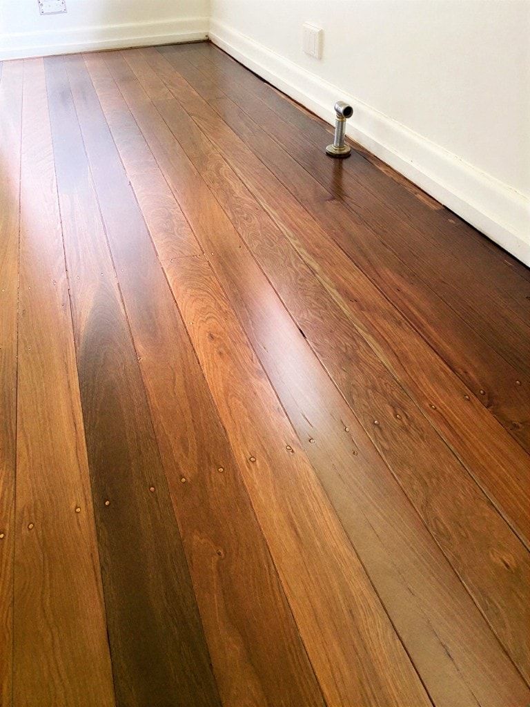 Satin-finish hardwood floor with honey-to-espresso boards, nail plugs, and a soft sheen beside a white skirting board